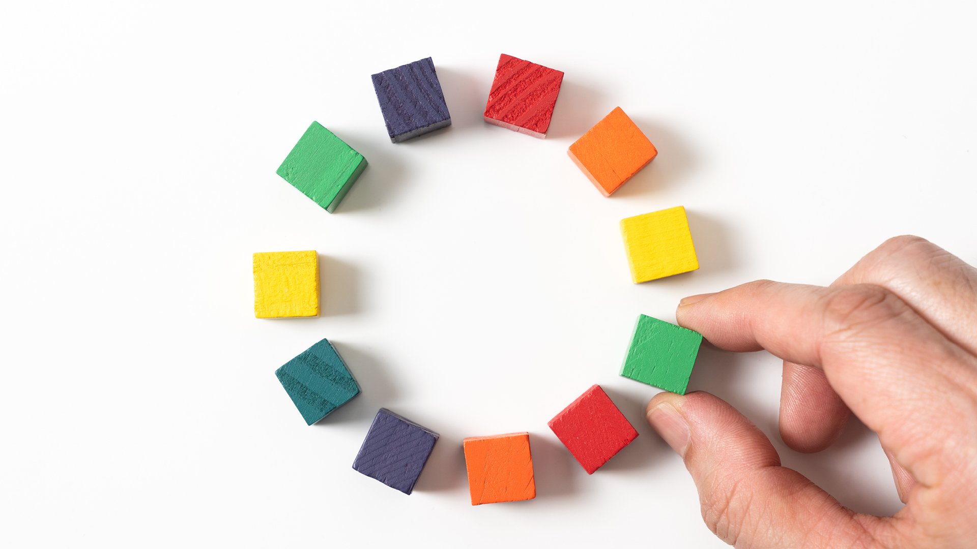 Hand arranging colorful wooden blocks in a circle representing the efficiency and organization achieved through centralized data in policy management.