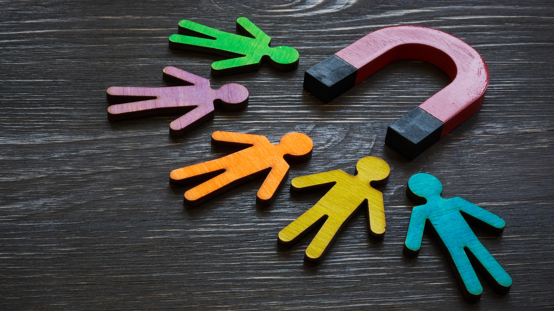 A large red and black magnet attracting colorful wooden figures, symbolizing strategies for driving customer loyalty in the workers' compensation industry.